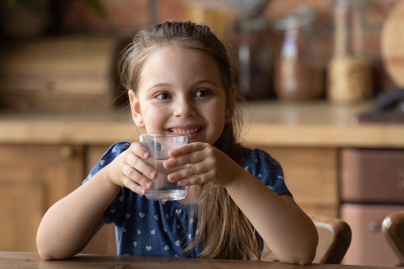 Young girl drinking water out of a glass and smiling